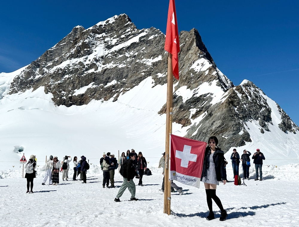 女生近距離在少女峰瑞士國旗旁拍照雪地