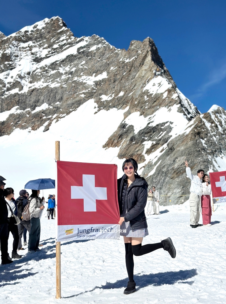 女生在少女峰雪地瑞士旗旁擺姿勢拍照